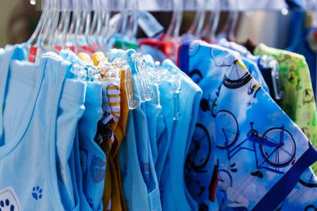 Baby clothes pants t-shirts sweaters shirts hanging on hangers in a shop outside in sunny weatherの写真素材
