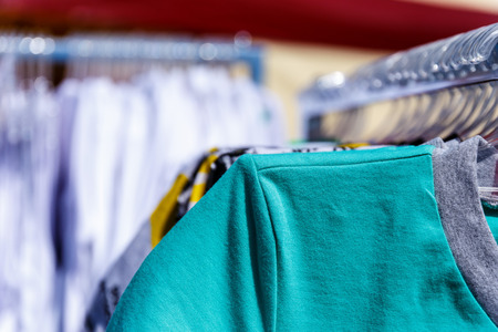 Baby clothes pants t-shirts sweaters shirts hanging on hangers in a shop outside in sunny weatherの写真素材