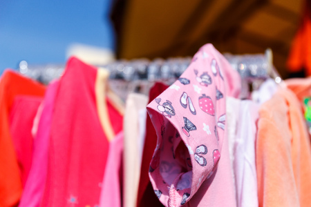 Baby clothes pants t-shirts sweaters shirts hanging on hangers in a shop outside in sunny weatherの写真素材