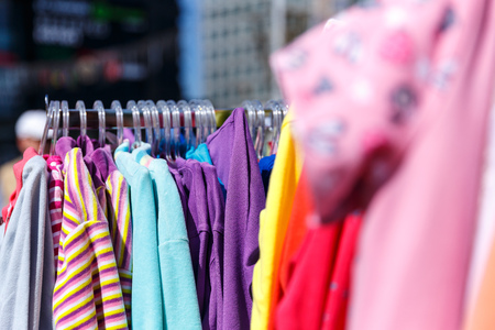 Baby clothes pants t-shirts sweaters shirts hanging on hangers in a shop outside in sunny weatherの写真素材