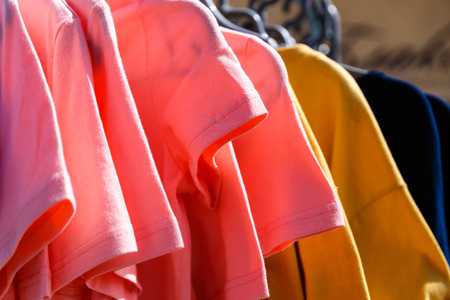 Baby clothes pants t-shirts sweaters shirts hanging on hangers in a shop outside in sunny weatherの写真素材