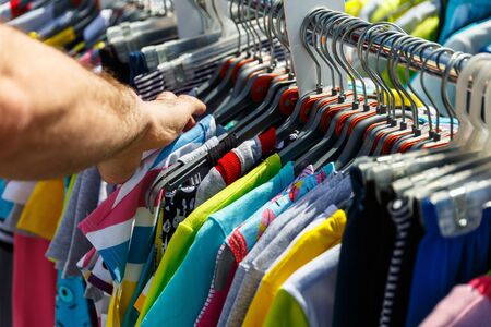 The hand chooses the clothes that hang on the hangers in the shop on the streetの写真素材