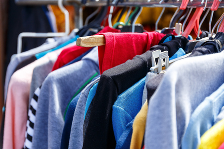 Men's and women's summer clothes sweatshirts shirts trousers jerseys coats jackets on the hanger in the shop on the streetの写真素材