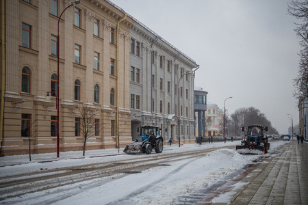 Tractor cleaning the road from the snow. Excavator cleans the streets of large amounts of snow in city. Workers sweep snow from road in winter, Cleaning road from snow storm.のeditorial素材
