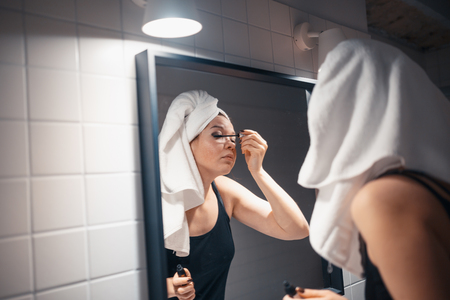 MINSK, BELARUS - MAY 1, 2017: Beautiful young woman applying makeup in front of her bathroom mirrorのeditorial素材
