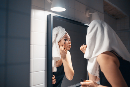 MINSK, BELARUS - MAY 1, 2017: Beautiful young woman applying makeup in front of her bathroom mirrorのeditorial素材