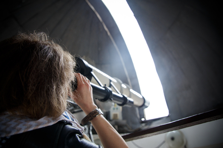 Young woman tourist looking through telescope on top in astronomic observatory