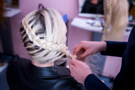 Young smiling cheerful positive hairdresser does to woman haircut with use of scissors and hairbrushes in hairdress salonの写真素材