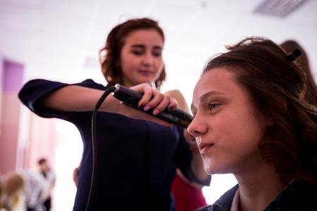 MINSK, BELARUS - AUGUST 1, 2017: Young smiling cheerful positive hairdresser does to woman haircut with use of scissors and hairbrushes in hairdress salonのeditorial素材