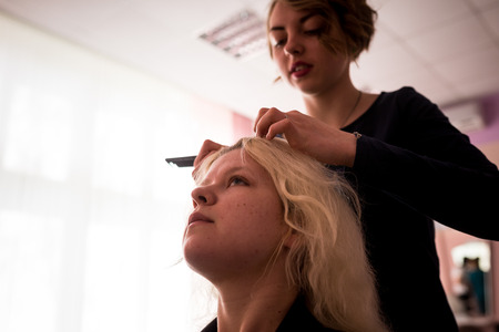 MINSK, BELARUS - AUGUST 1, 2017: Young smiling cheerful positive hairdresser does to woman haircut with use of scissors and hairbrushes in hairdress salonのeditorial素材