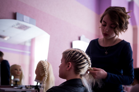 MINSK, BELARUS - AUGUST 1, 2017: Young smiling cheerful positive hairdresser does to woman haircut with use of scissors and hairbrushes in hairdress salonのeditorial素材