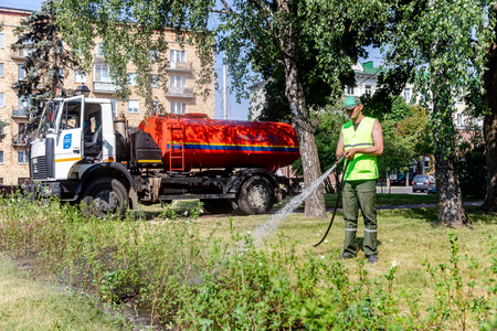 MINSK, BELARUS - 1 JUNE, 2019: utility worker gardener of municipality with hose for watering the plants and trees in city parkのeditorial素材