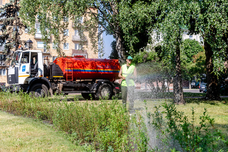 MINSK, BELARUS - 1 JUNE, 2019: utility worker gardener of municipality with hose for watering the plants and trees in city parkのeditorial素材