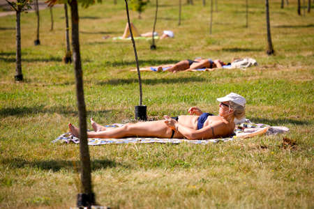 MINSK, BELARUS - 9 AUGUST, 2020: people sunbathe in the city park in sunny hot weatherの写真素材
