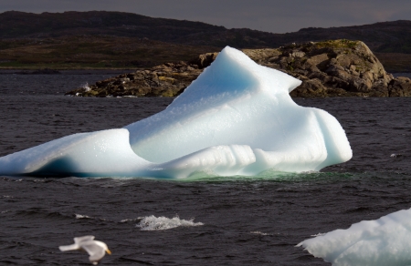 Bright white iceberg on dark water and rock 