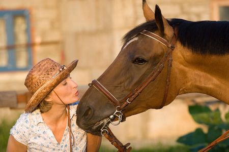 Woman in hat kissing brown horseの写真素材
