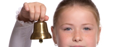Young school girl ringing a golden bell on white background focused on bellの写真素材