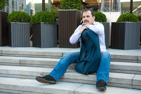 Adult sad man sitting on stears in front of cafe entrance