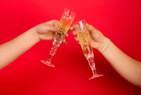 Glass of champagne in the womans hands on red backgroundの写真素材
