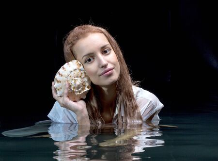Pretty girl holds a shell in his hands looking out at the water