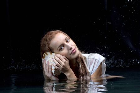 Pretty girl holds a shell in his hands looking out at the waterの写真素材