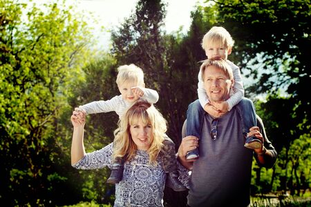 Happy family, kids on pearents shoulder. Coloring and processing photos in vintage style with soft selective focusの写真素材