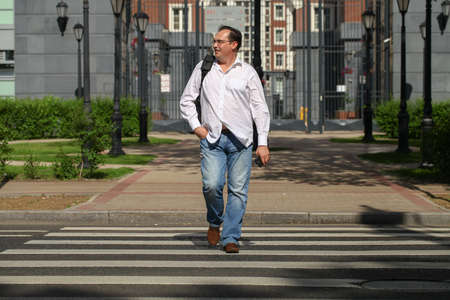 Man in casual dress crossing the road with classic English building on backgroundの写真素材