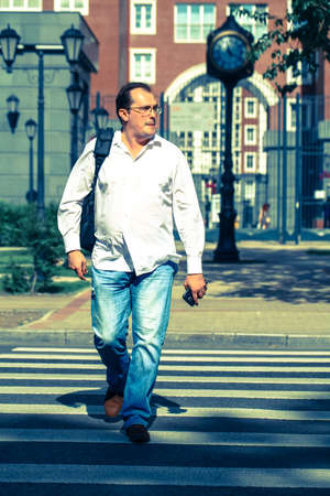 Man in casual dress crossing the road with classic English building on background. Vintage concept,...