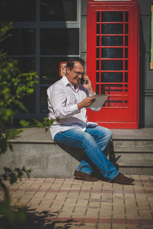 Business man using mobile phone red classic English telephone boxの写真素材