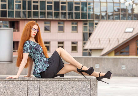 Redhead woman sitting on marble on urban backgroundの写真素材