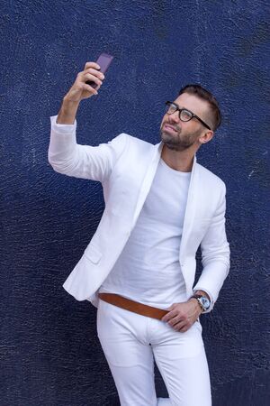 Hipster fashion man, street style, blogger. Man in white suit on blue wall background.