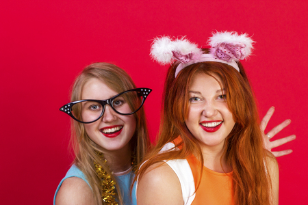 Young nice girls have fun on a christmas party. On red background.の写真素材