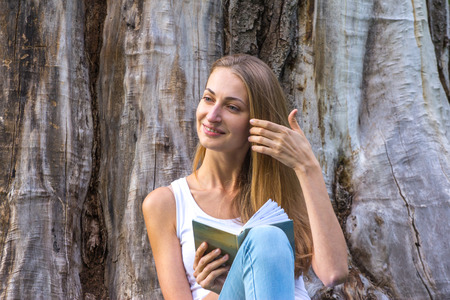 Young woman sitting on the grass and reading book outdoor.