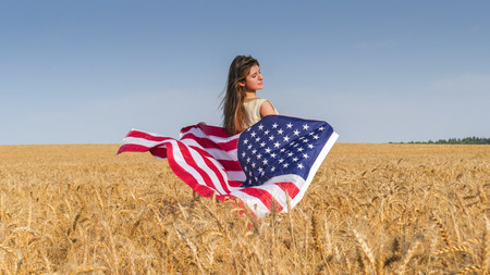 Beautiful brunette girl in natural linen dress  with a US flag in the fieldの写真素材