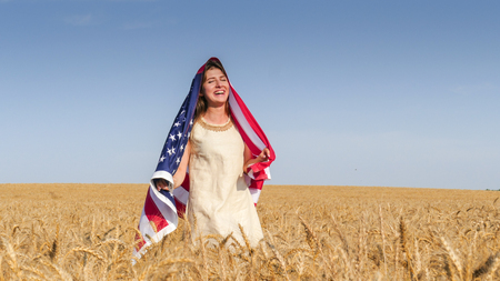 Beautiful brunette girl in natural linen dress  with a US flag in the fieldの写真素材