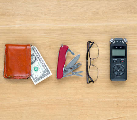 Journalist travel set on the table. Voice recorder, knife, wallet, banknotes, glasses.