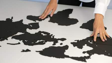 Women's hands touch the parts of the world map on the desk in the officeの写真素材