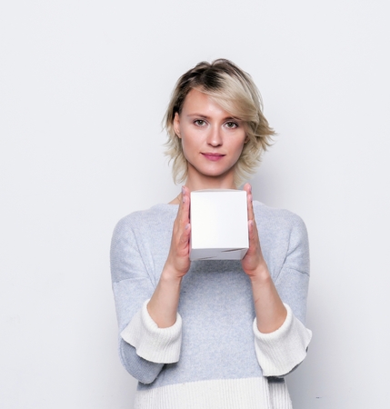 Happy girl giving small white gift box. Small gift in the hands of a woman indoor.の写真素材
