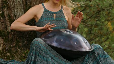 Popular, modern hang musical instrument in the hands of a beautiful blonde in an autumn park.
