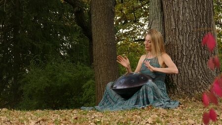 Beautiful young woman plays a hangpan in the autumn park