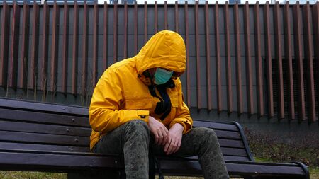Sick man in yellow jacket and medical mask falls on a bench without strength from illness. death conceptの写真素材