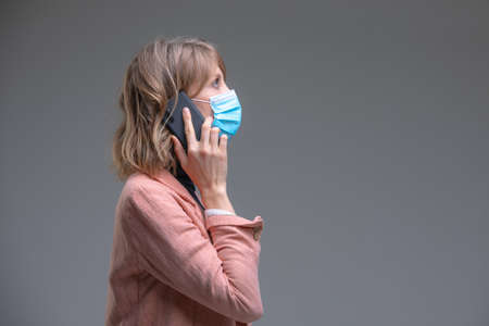 Gorgeous blond young female with wearing protective mask against viruses, mobile phone speaking