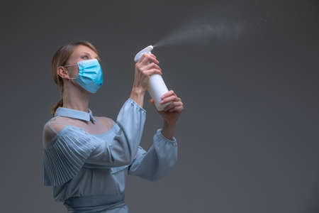 Housekeeper in vintage blue dress and protective mask with spray bottle. Disinfection, cleaning, aromatization conceptの写真素材