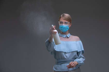 Housekeeper in vintage blue dress and protective mask with spray bottle. Disinfection, cleaning,...