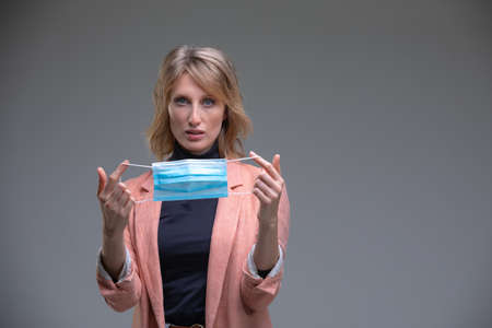 Head portrait attractive blond woman hold her surgical mask protecting from COVID19 or corona virus....