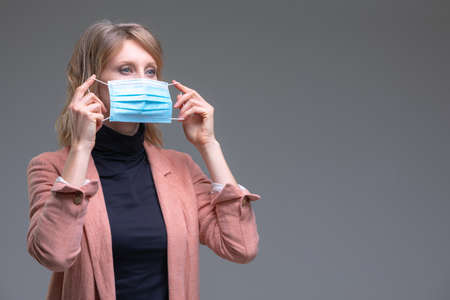Head portrait attractive blond woman hold her surgical mask protecting from COVID19 or corona virus. Personal care during pandemic infectious. End of pandemia concept.の写真素材