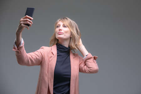 Portrait of cool cheerful woman having video-call with lover holding smart phone in hand shooting...