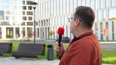 Adult journalist with microphone working in autumn park.の写真素材