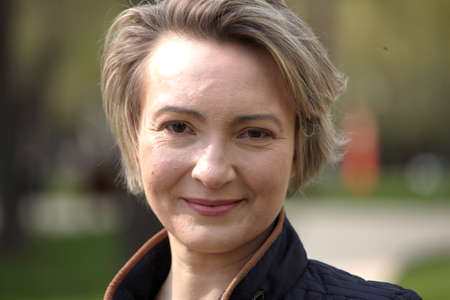 Beautiful mid age woman close-up portrait in modern casual wear, against green of summer park.の写真素材