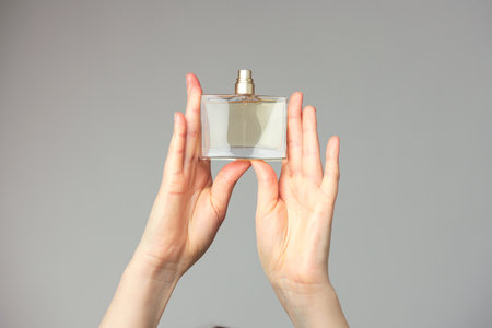 Perfume bottle in beautiful woman hands on grey backgroundの写真素材